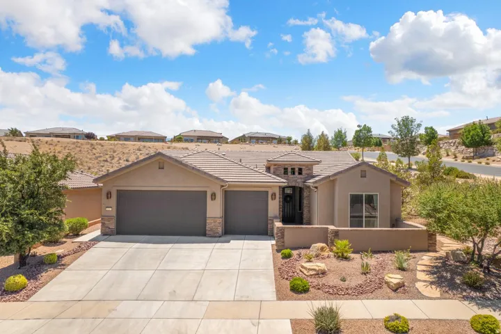 Stucco exterior with stone accents, two-car garage, concrete driveway, and desert-inspired landscaping