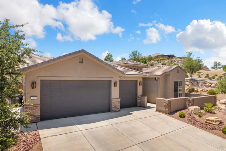 Contemporary stucco exterior with a tiled roof, multi-car garage, stone accents, and a concrete driveway