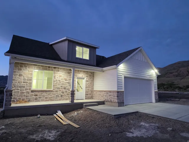 Exterior featuring a stone facade, white siding accents, a covered front porch with columns, a prominent two-car garage, and a dormer with vertical siding