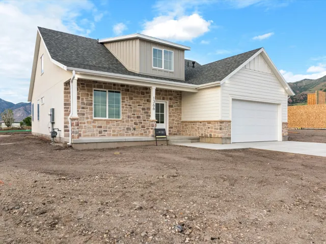 Contemporary dwelling featuring a stone and siding facade, covered front porch, attached garage with white door, and a dormer window