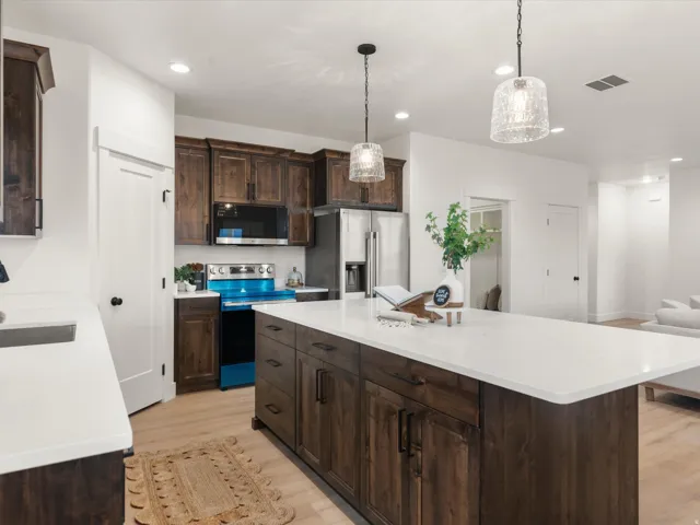 Kitchen featuring a large island with a white countertop, dark wood-finish cabinetry, stainless steel appliances, and two pendant light fixtures