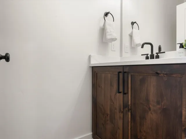 Dark wood-finish vanity featuring matte black hardware, a white countertop, and a contemporary matte black faucet