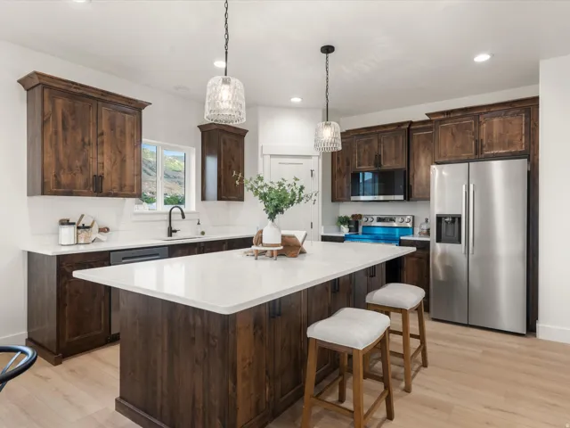 Kitchen featuring a central island with white countertop, dark wood-finish cabinetry, stainless steel appliances, and light wood-finish flooring