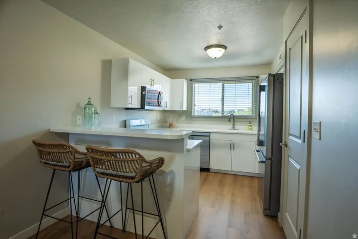 Kitchen featuring white cabinetry, light-toned countertops, stainless steel appliances, wood-finish flooring, and a breakfast bar