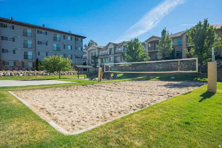 Sand volleyball court featuring a net and padded posts, surrounded by green lawn