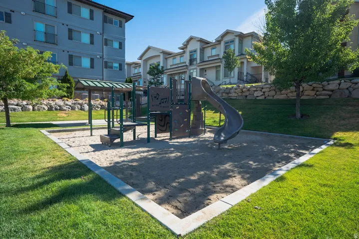 Outdoor playground area featuring a sand base, a slide, climbing elements, and a covered structure