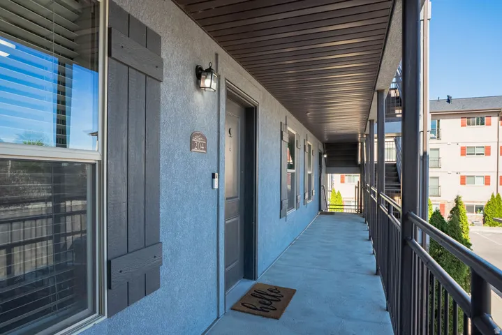 Covered exterior walkway featuring a textured stucco finish, dark board-and-batten style shutters, and an overhead light fixture