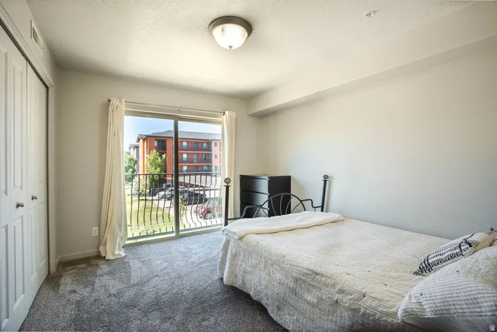 Sliding glass door with wrought iron railing, plush grey carpeting, and white bi-fold closet doors