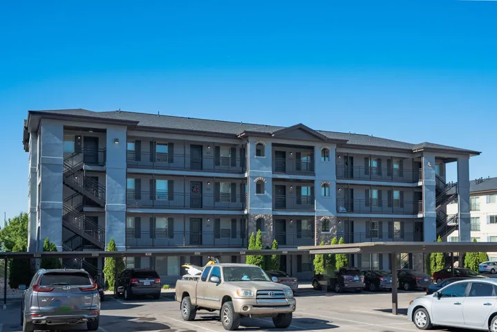Multi-story residential building featuring a gray stucco exterior, dark composite shingle roof, and stone facade accents