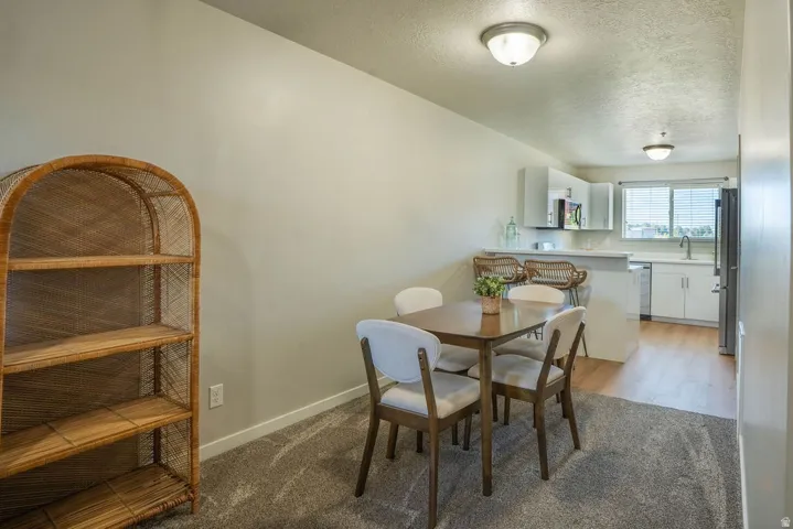 Dining area featuring carpet flooring, overhead lighting, and an open layout into the kitchen with wood-finish flooring, white cabinetry, and stainless steel appliances