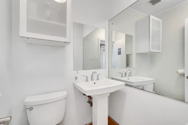 Pedestal sink with chrome faucet, full-wall mirror, and wall-mounted storage cabinet