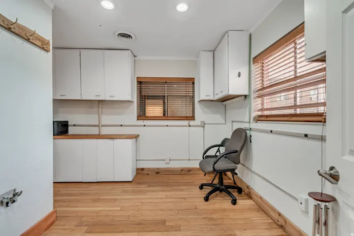 Spacious interior room featuring wood-finish flooring, white cabinetry with wood countertops, and multiple windows with wood blinds