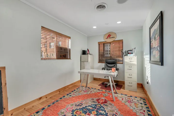 Room with light-toned walls, wood-finish flooring, and two windows featuring wood slat blinds
