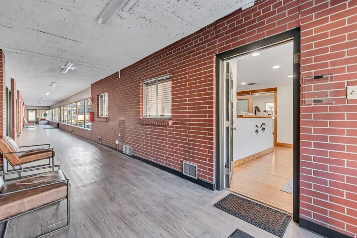 Long hallway featuring brick walls, wood-finish flooring, and multiple windows with blinds