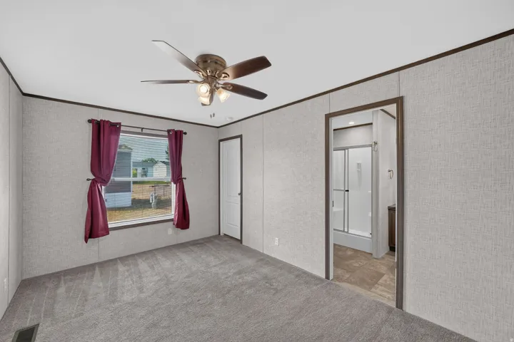 Spacious room featuring gray textured wall panels with dark trim, a ceiling fan with integrated lighting, and neutral carpet flooring