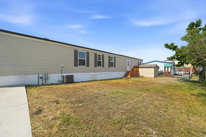 Exterior featuring tan horizontal siding, dark window shutters, white trim, a concrete walkway, and an outdoor storage shed