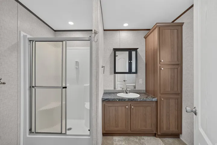 Bathroom featuring a white shower with sliding glass doors, a wood-finish vanity with a single basin sink, a dark countertop, and a matching wood-finish storage cabinet