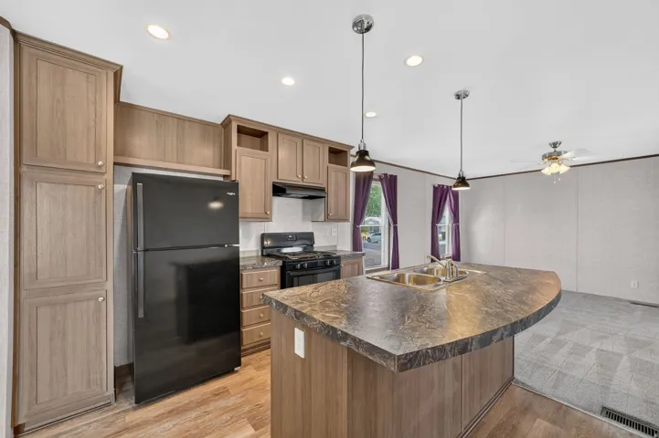 Kitchen featuring a breakfast bar island with double sink, black appliances, recessed lighting, wood-finish flooring, and light-toned cabinetry
