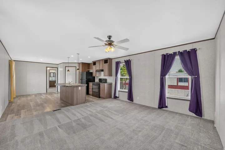 Open-concept living space featuring a ceiling fan, windows with natural light, and a kitchen island with pendant lighting