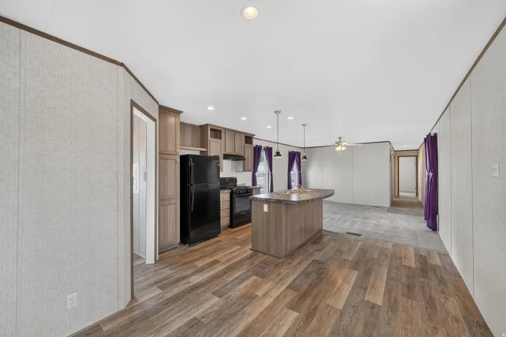Open concept kitchen featuring dark wood-finish cabinetry, black appliances, a central island with a curved countertop, and pendant lighting