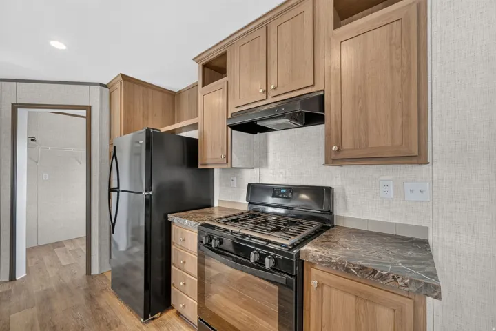 Kitchen featuring wood-finish cabinetry, dark countertop, black gas range, and black refrigerator