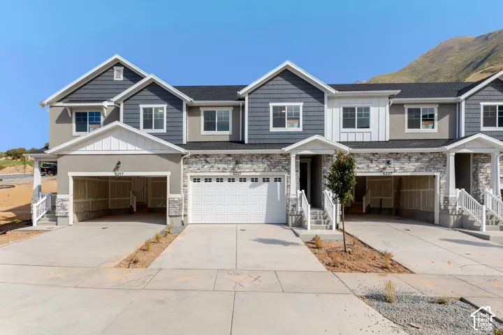 Multi-unit exterior featuring composite shingle siding, natural stone veneer facade, multiple gabled rooflines, and attached garage bays