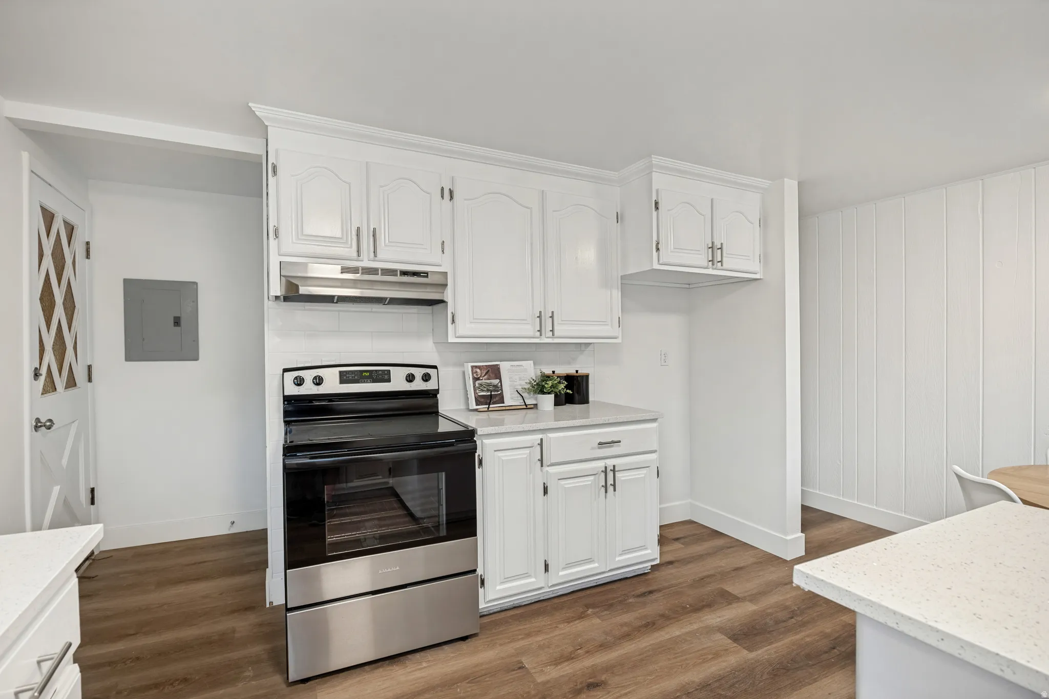 Kitchen featuring white cabinetry, a stainless steel range with overhead ventilation, light-toned countertops, and wood-finish flooring