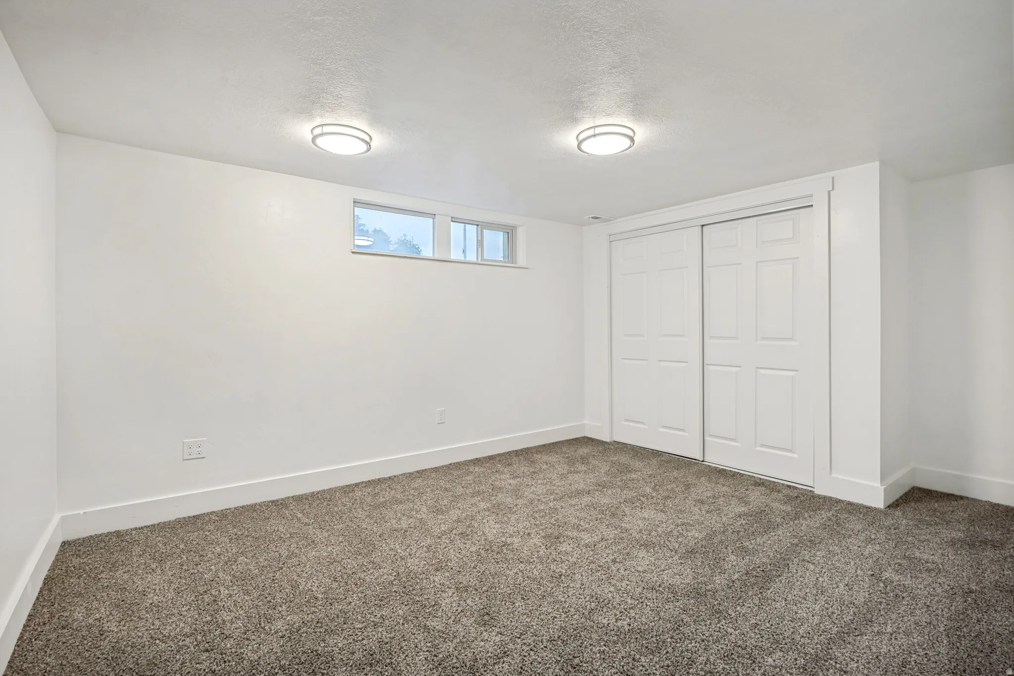 Carpeted room featuring white walls, baseboards, and a sliding closet door