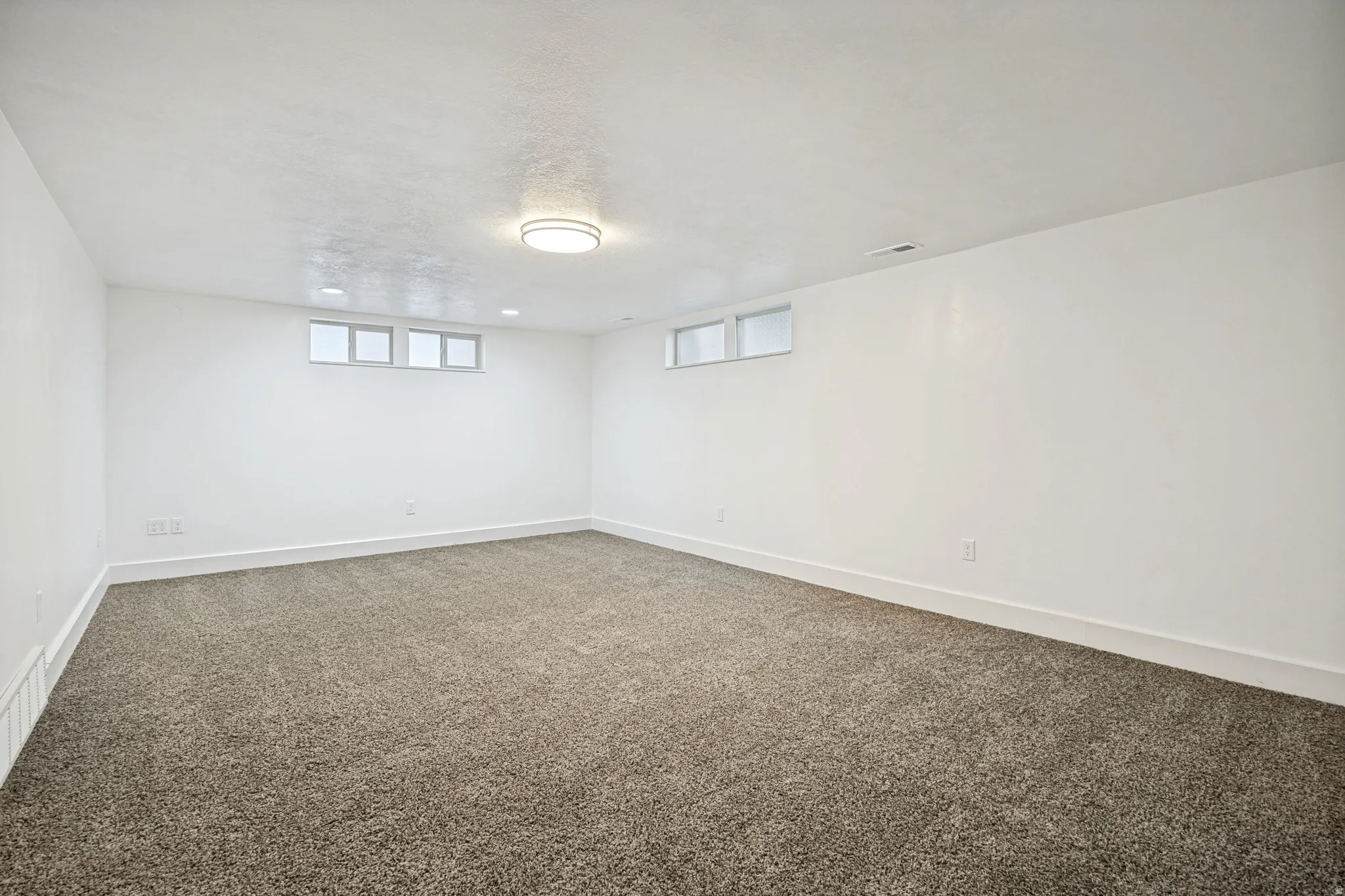 Spacious room with new carpeting, white walls, and bright overhead lighting