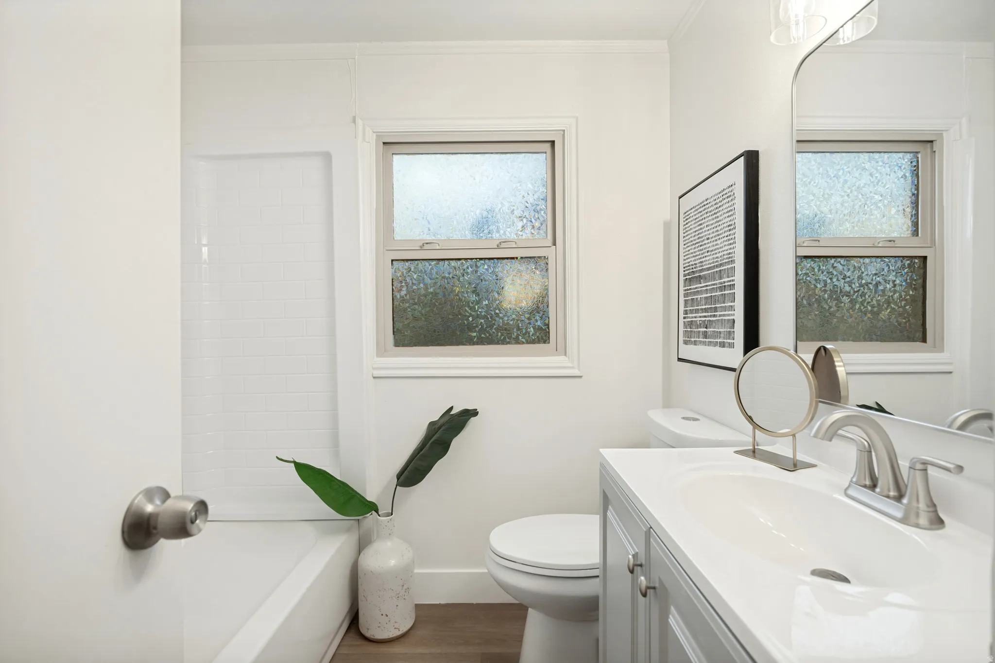 Bathroom featuring a white subway tile tub surround, double windows with privacy glass, a vanity with an integrated sink, and wood-finish flooring