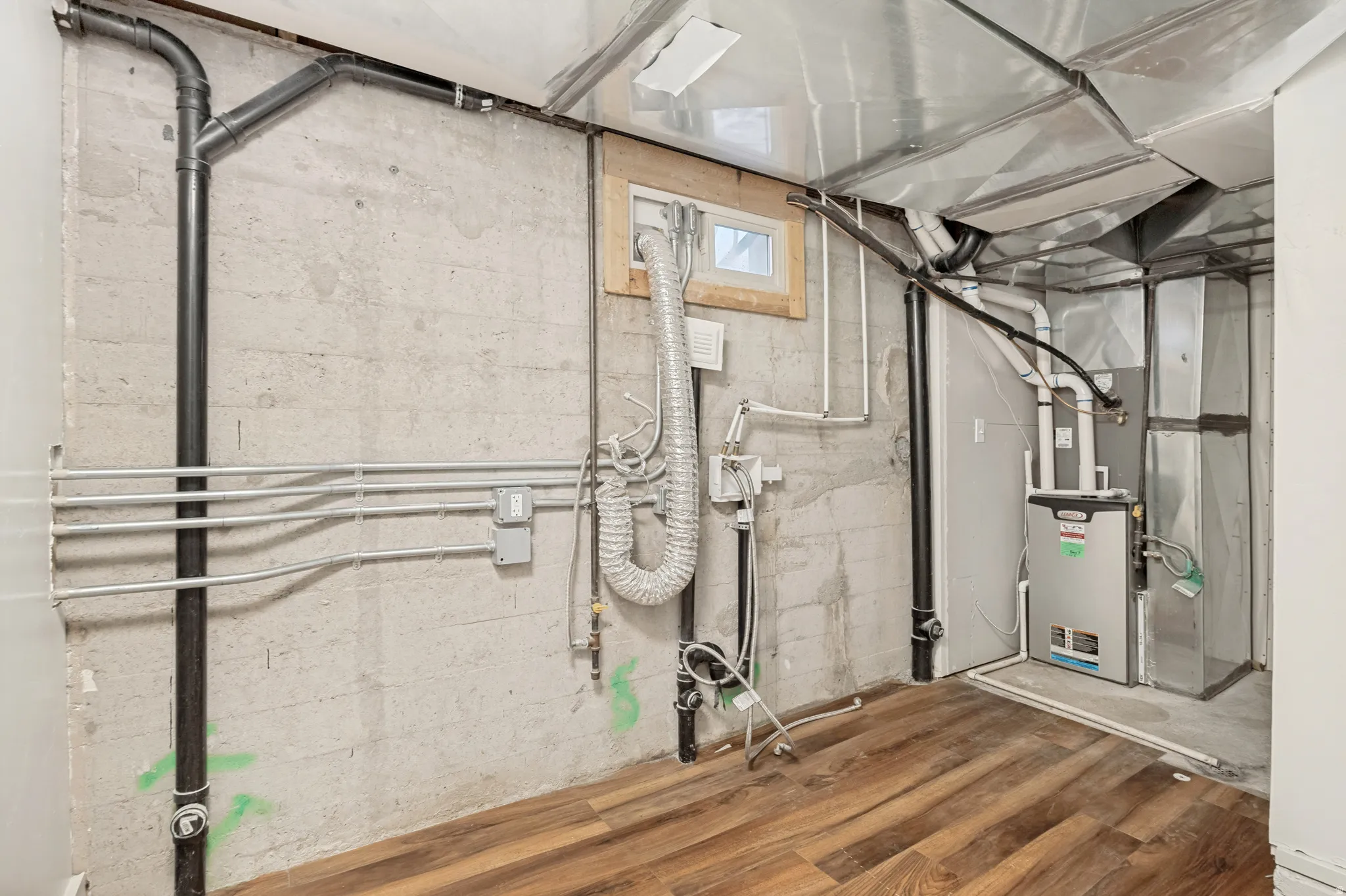 Finished basement area featuring wood-finish flooring, exposed concrete walls, a single window, and visible HVAC ductwork