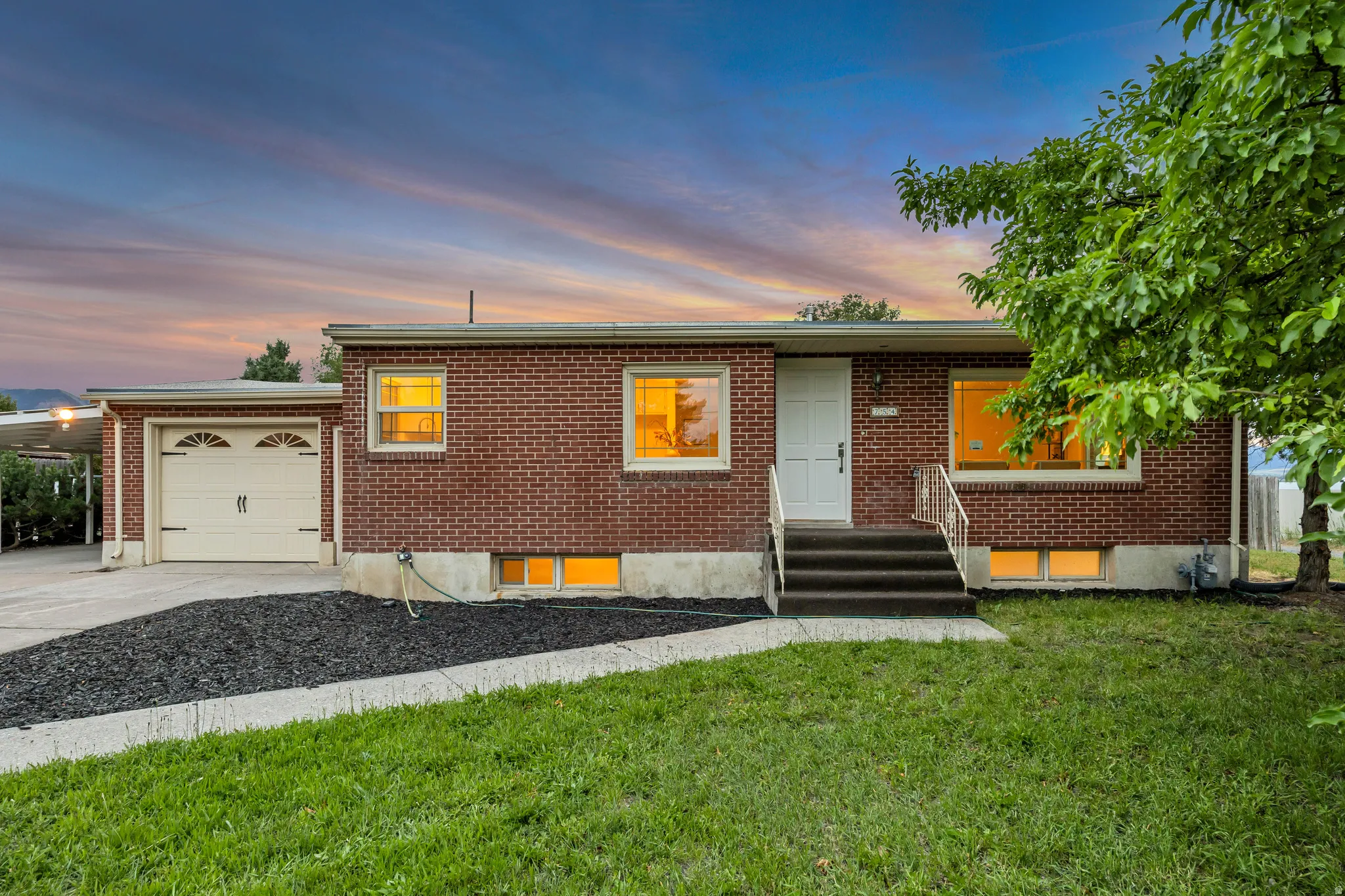 Brick-clad residence featuring a single-car garage with an arched door, a covered carport, and a concrete driveway