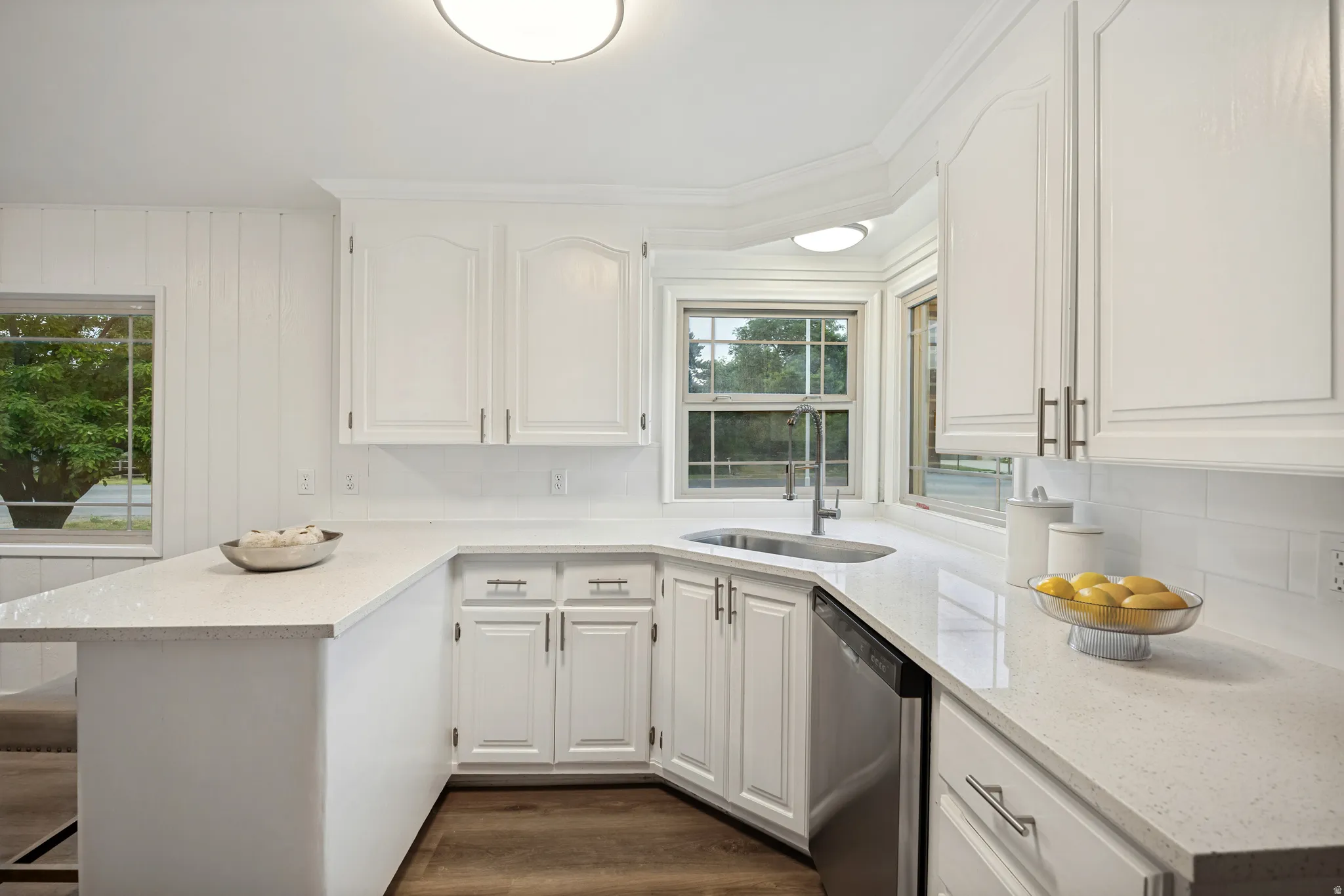 Contemporary kitchen featuring white cabinetry, light-toned countertops, a stainless steel sink, a stainless steel dishwasher, and wood-finish flooring