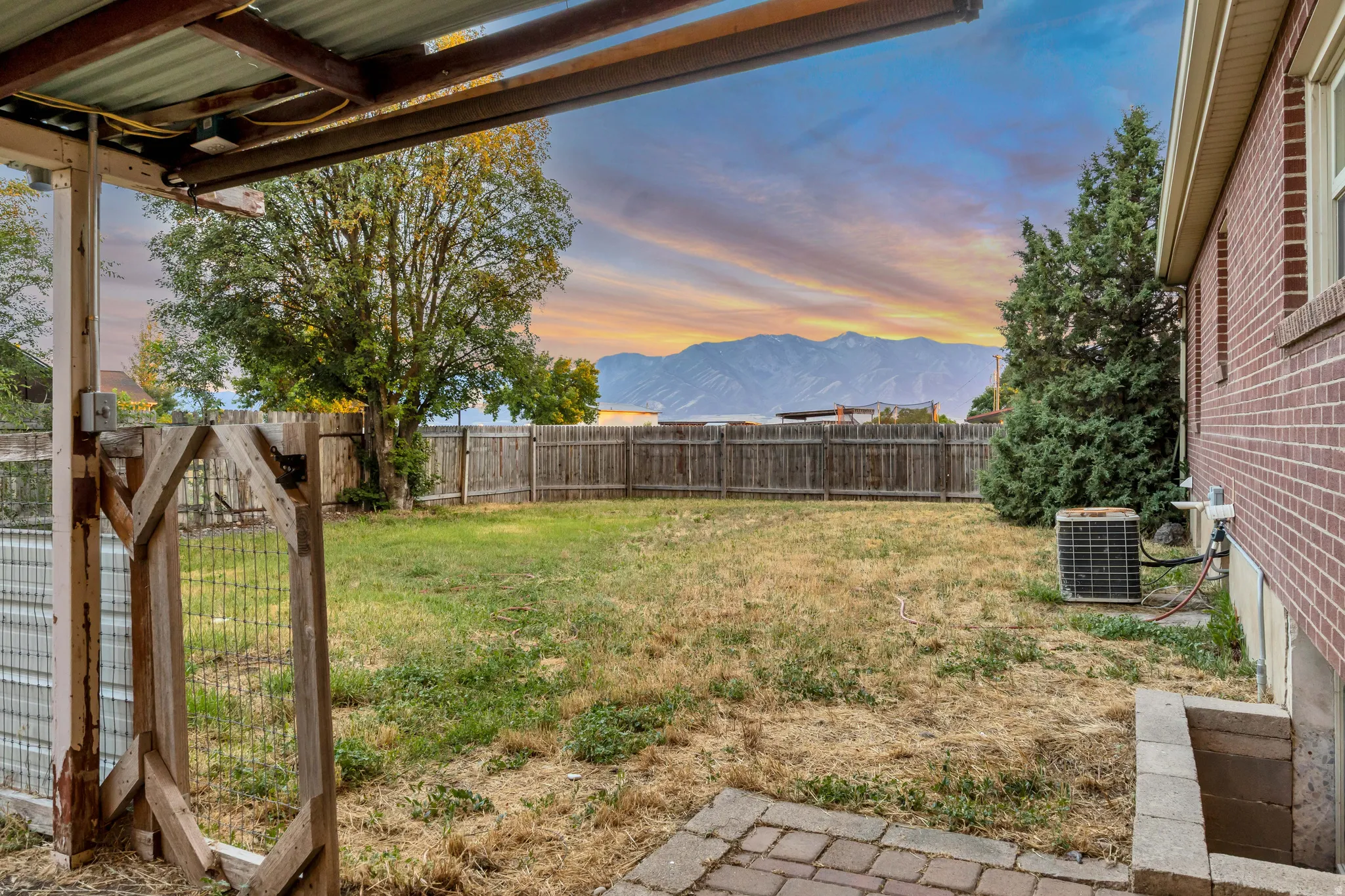 Expansive backyard with a full perimeter wood fence, mature trees, brick exterior, and a mountain backdrop
