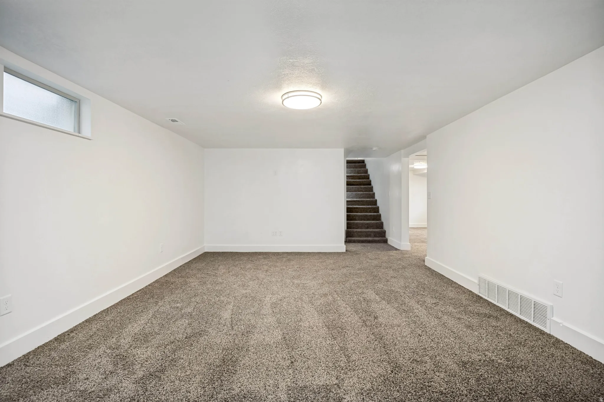 Expansive room featuring plush gray carpeting, white painted walls, and white baseboards