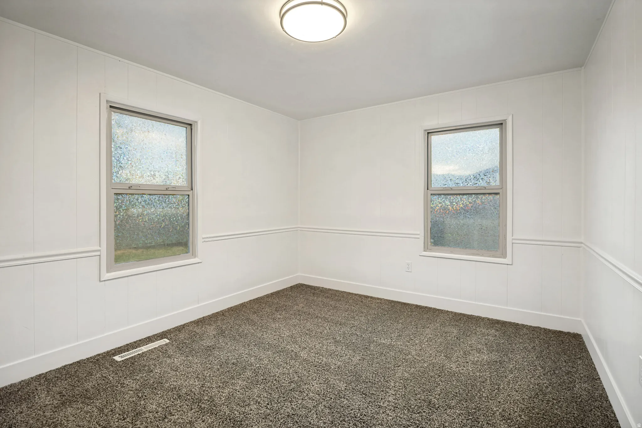 Room featuring two single-hung windows, white paneled walls, white trim, and gray carpet flooring