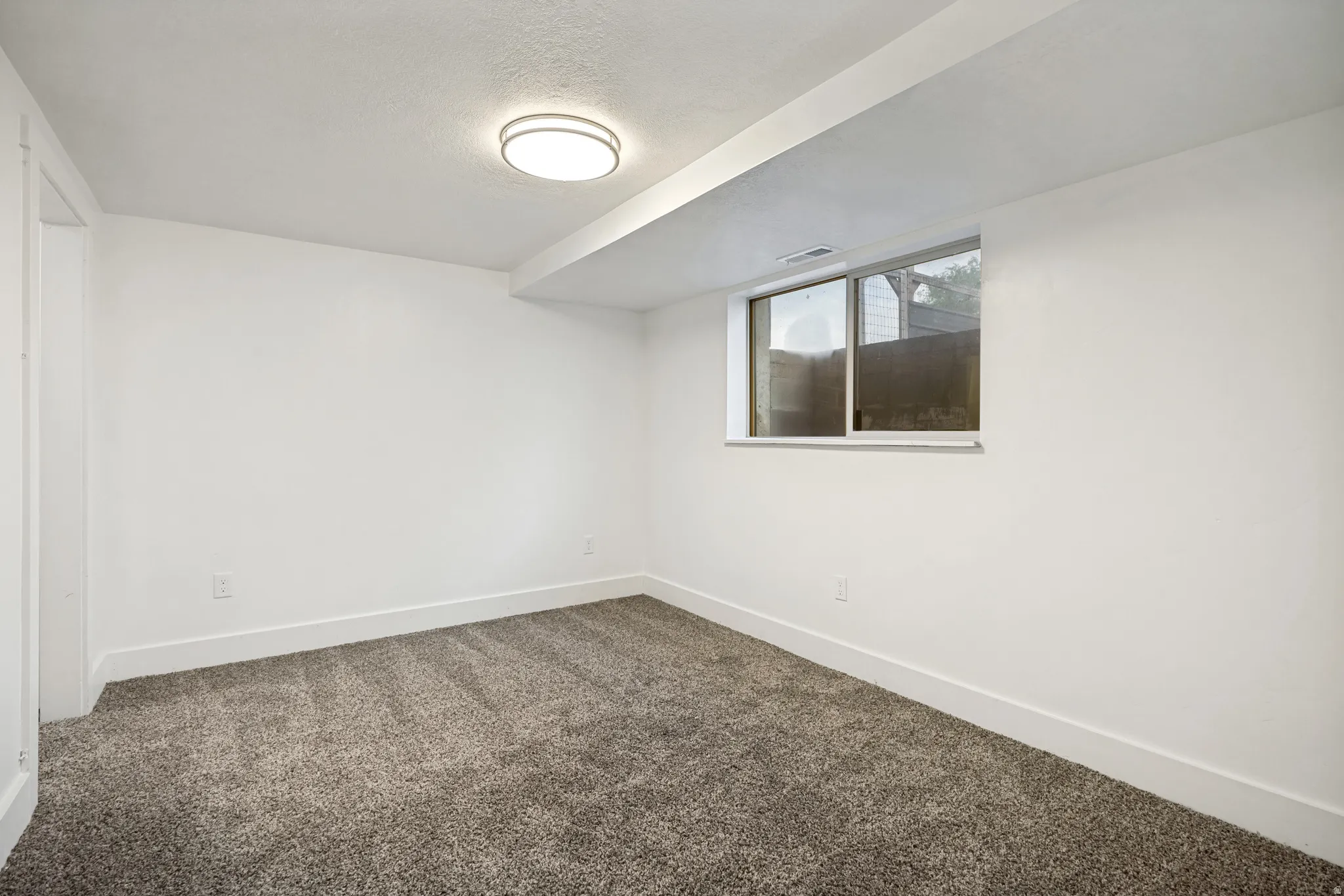 Carpeted room featuring a white ceiling and walls, a flush-mount ceiling light, a horizontal sliding window, and white baseboards