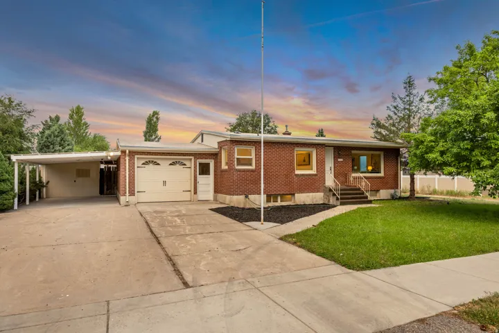 Brick exterior featuring a front lawn, attached garage, and a covered carport