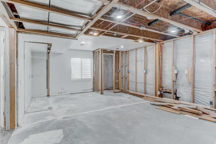 Unfinished interior space featuring exposed wood framing, a concrete slab floor, and a window with horizontal blinds