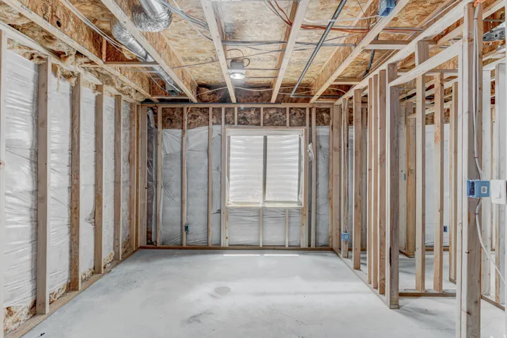 Unfinished lower level featuring concrete flooring, exposed wood framing, and a window with horizontal blinds