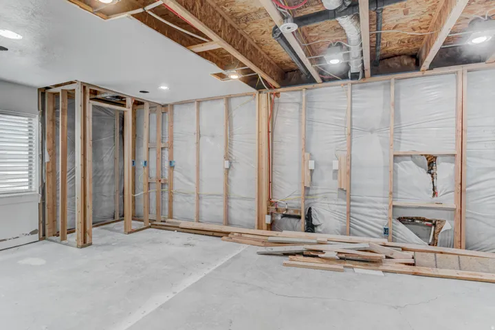 Basement interior featuring exposed wood framing, concrete flooring, recessed lighting, and a white window with horizontal blinds