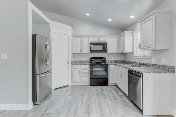 Modern kitchen featuring light wood-finish flooring, white cabinetry, speckled countertops, and stainless steel appliances