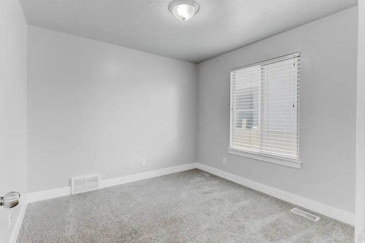 Carpeted room featuring a single window with blinds, light gray walls, white baseboards, and a flush-mount ceiling light fixture