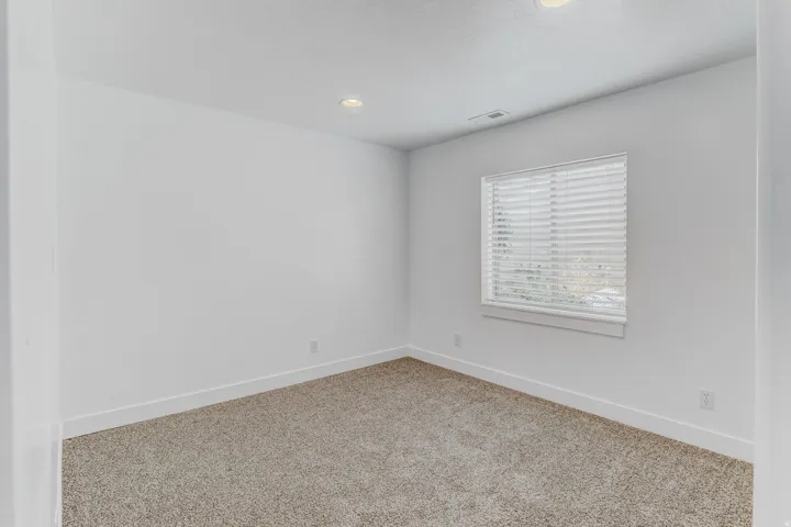 Bright room featuring neutral-toned carpeting, white walls, and a window with blinds