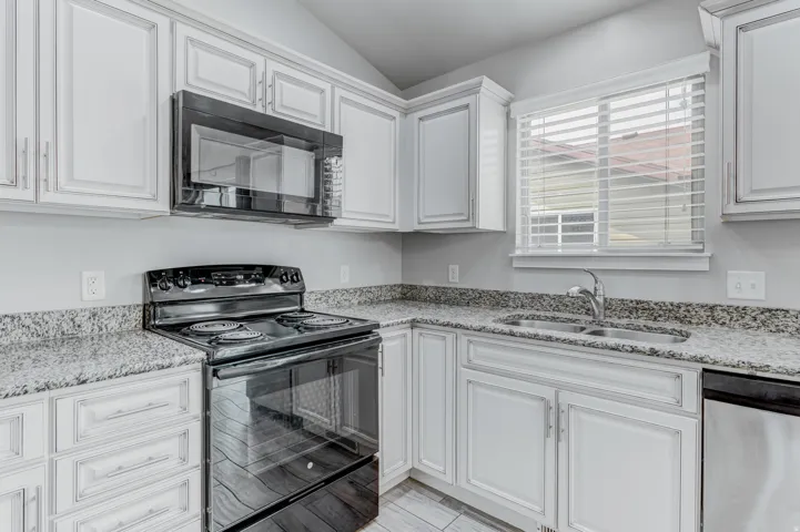 Kitchen featuring white cabinetry, granite countertops, a black range, an over-the-range microwave, and a stainless steel dishwasher