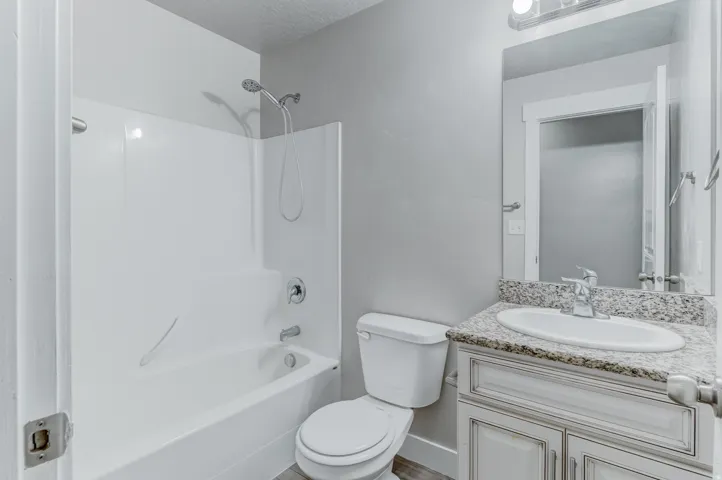Bathroom featuring a white tub-shower combination, a vanity with a light-toned countertop, a rectangular mirror, and light gray wall paint