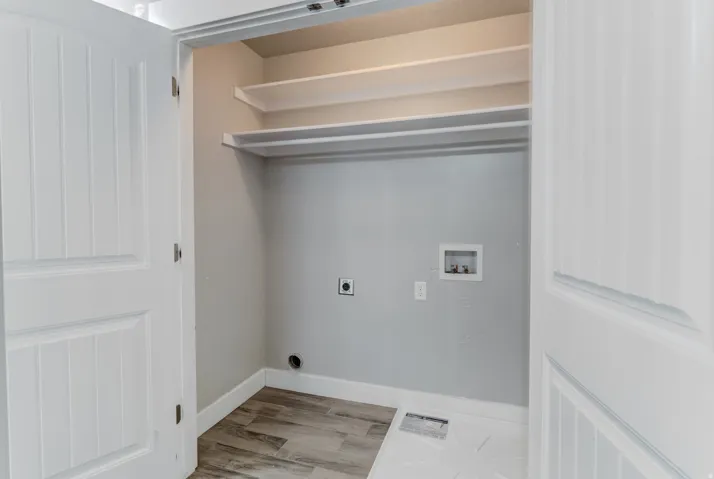 Laundry area featuring wood-finish flooring, two white shelving units, and a clothes hanging rod