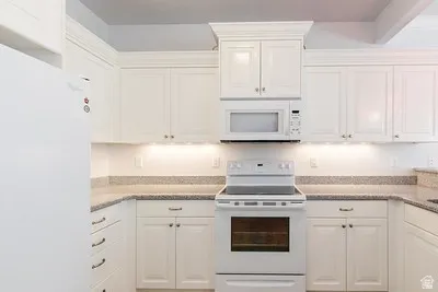 U-shaped kitchen featuring white cabinetry, light-toned countertops, a built-in microwave, and an electric range with an oven