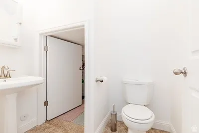 Bathroom featuring a pedestal sink with brushed nickel faucet, a white toilet, and neutral-toned floor tiling