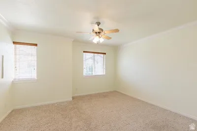 Carpeted room featuring two windows with horizontal blinds, a ceiling fan with integrated lighting, and crown molding